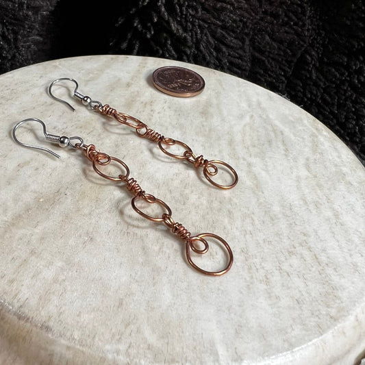 Handmade copper wire spiral chain earrings with circular links and surgical steel ear wires, photographed with Canadian penny for scale.