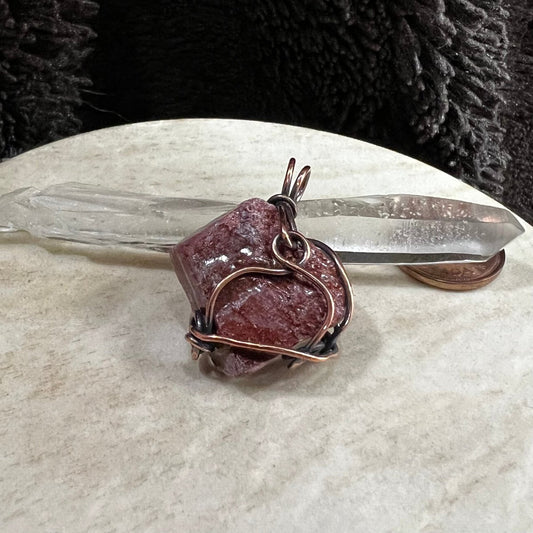 red calcite pendant wrapped in reclaimed copper with natural rough texture, handmade grounding crystal necklace on neutral background