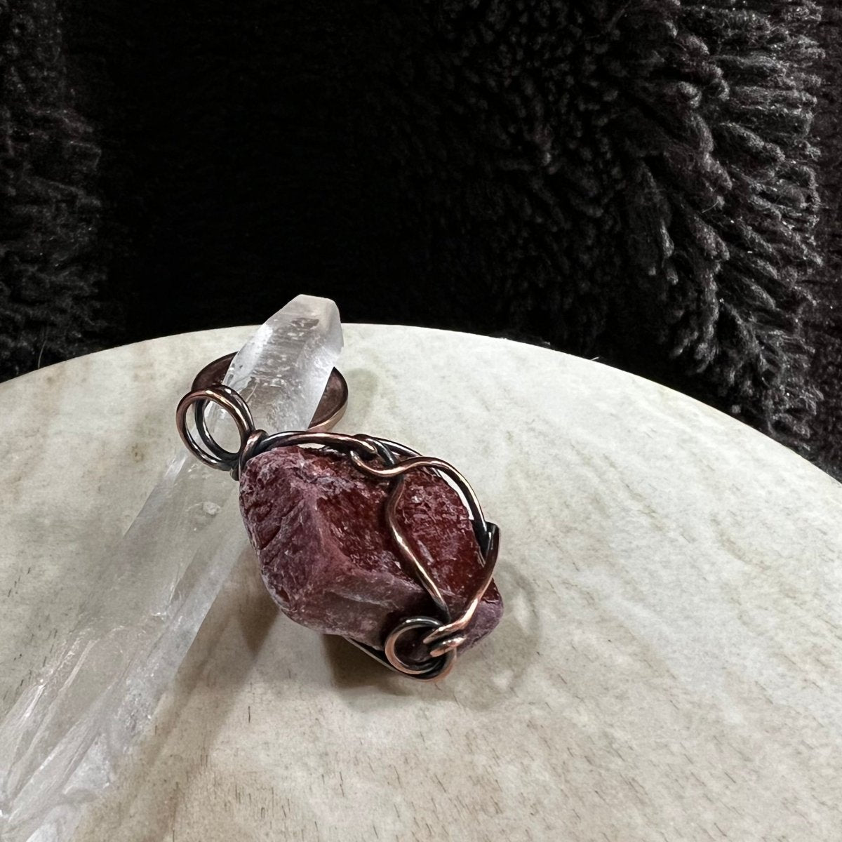 Copper wire-wrapped red calcite pendant on a white surface with a dark textured background