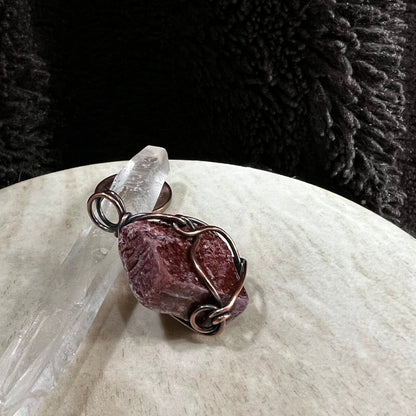 Copper wire-wrapped red calcite pendant on a white surface with a dark textured background
