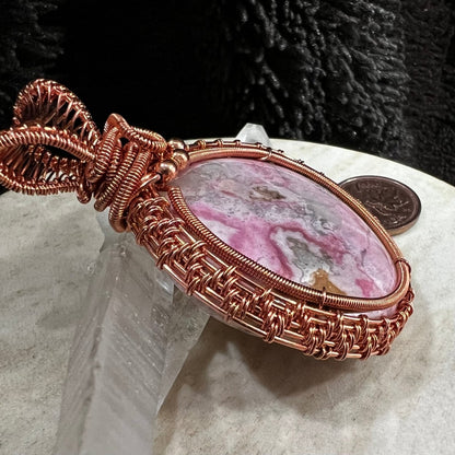 Close up of copper wire weaving on a rhodochrosite pendant. Pink and cream natural patterns, handmade heart healing crystal necklace on neutral background