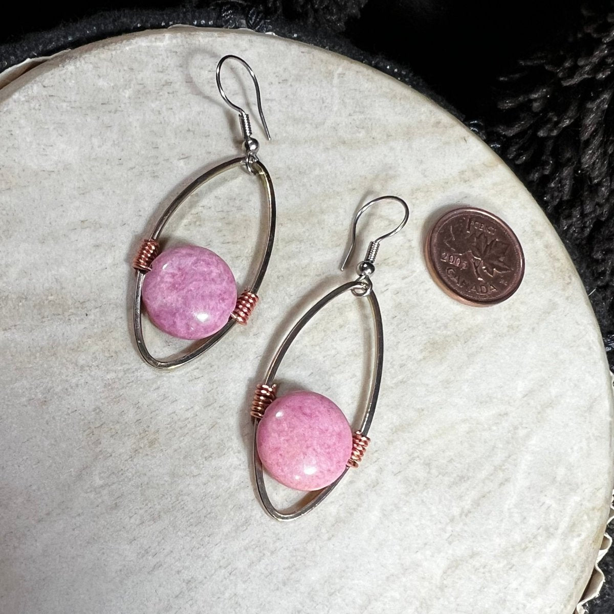 Handmade rhodochrosite bead earrings suspended in reclaimed silver-plated oval hoops with copper wire accents and surgical steel ear wires, photographed with Canadian penny for scale.