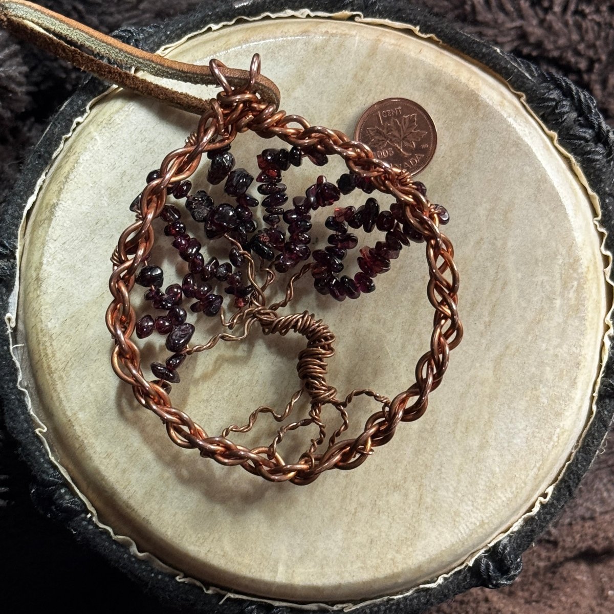 Back view of a garnet Tree of Life formed from reclaimed copper, showing its woven circular frame, twisted trunk and exposed roots.