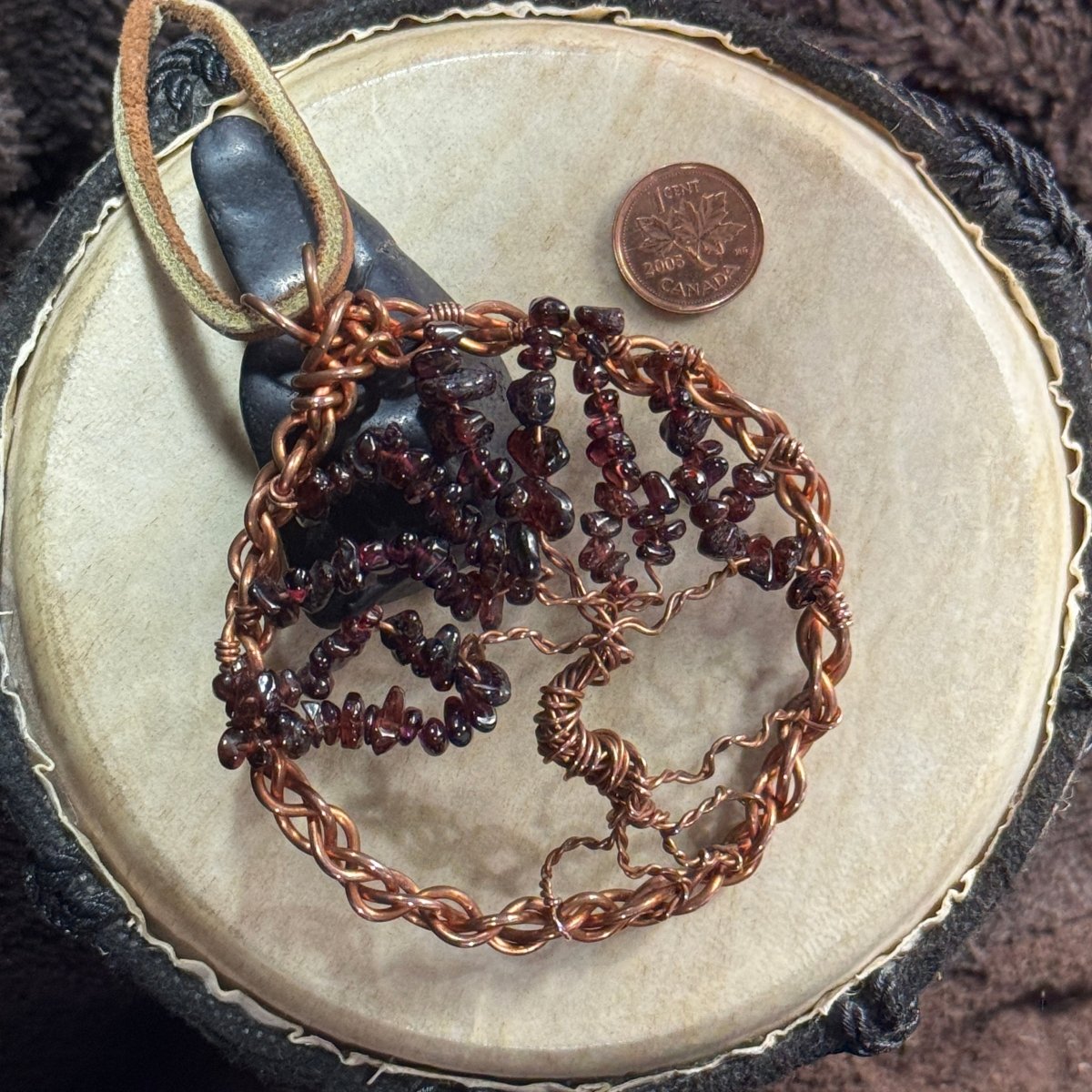 Garnet and reclaimed copper Tree of Life suncatcher styled beside a black shungite stone and Canadian penny; photographic props not included.