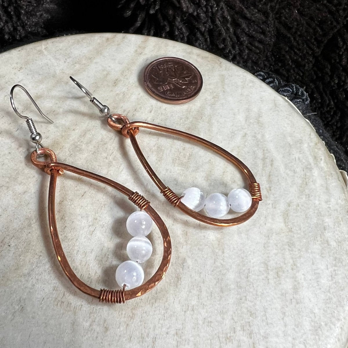 Handmade copper teardrop earrings with round selenite beads and surgical steel ear wires, photographed with Canadian penny for scale.