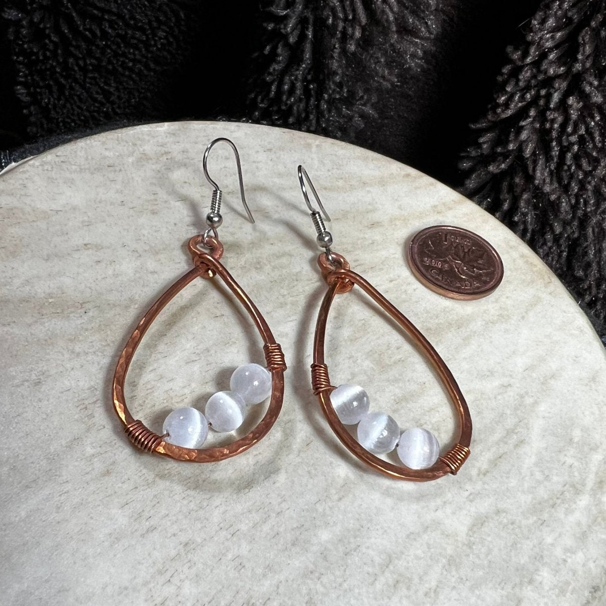 Handmade copper teardrop earrings with round selenite beads and surgical steel ear wires, photographed with Canadian penny for scale.