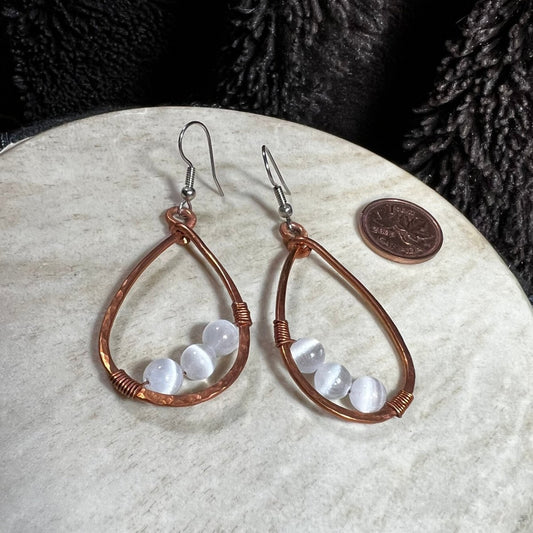 Handmade copper teardrop earrings with round selenite beads and surgical steel ear wires, photographed with Canadian penny for scale.