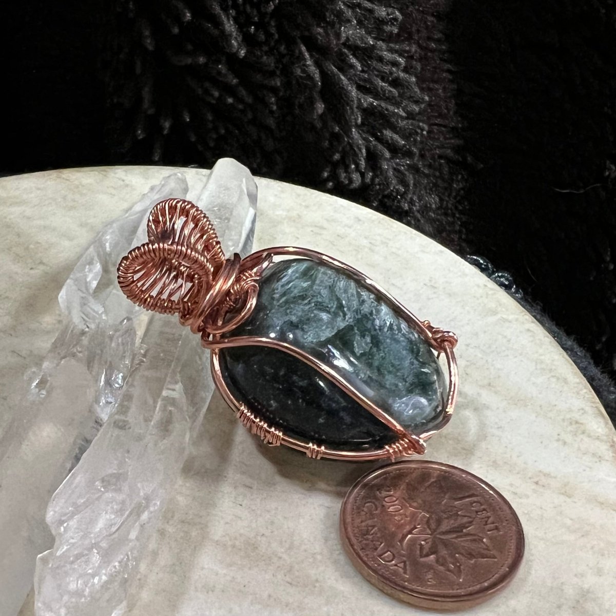 Copper-wrapped stone pendant with a coin on a marble surface