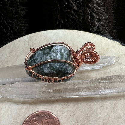 Copper-wrapped seraphinite stone pendant on a crystal with a Canadian penny for scale