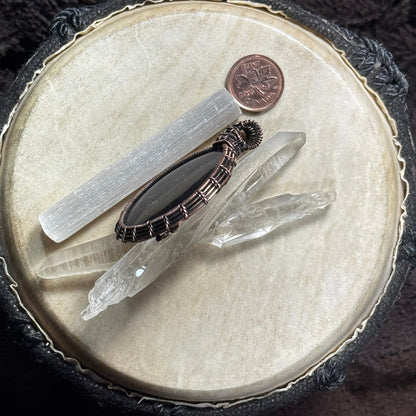 Side profile of a handcrafted shungite pendant displayed with crystal points, showing the depth of the stone and fine woven copper setting.
