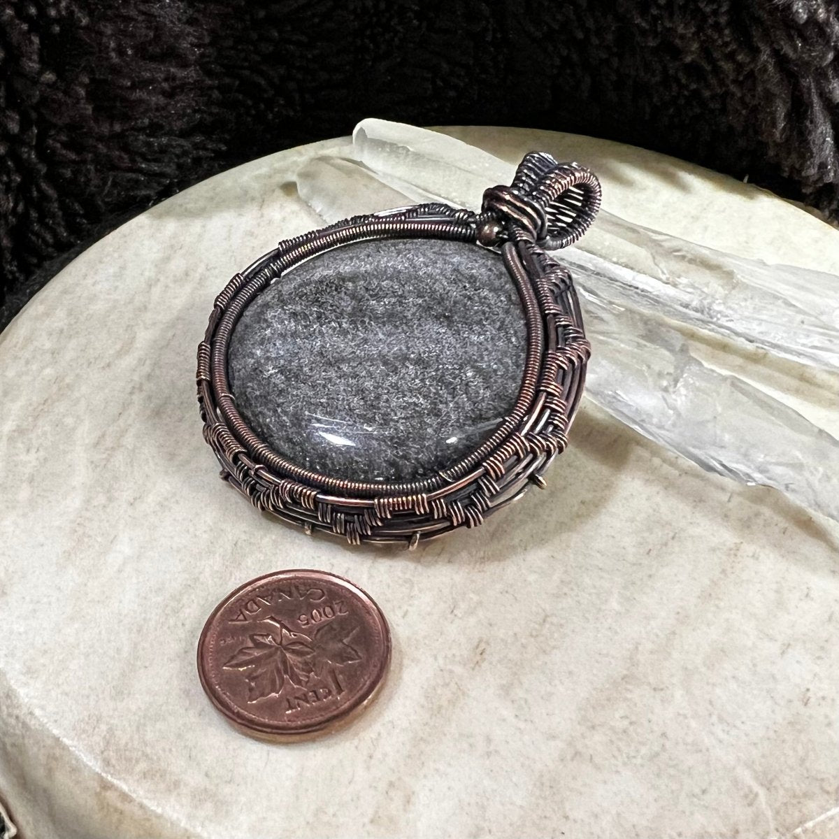 Side angle of copper-wrapped obsidian pendant highlighting structured wirework and patina finish