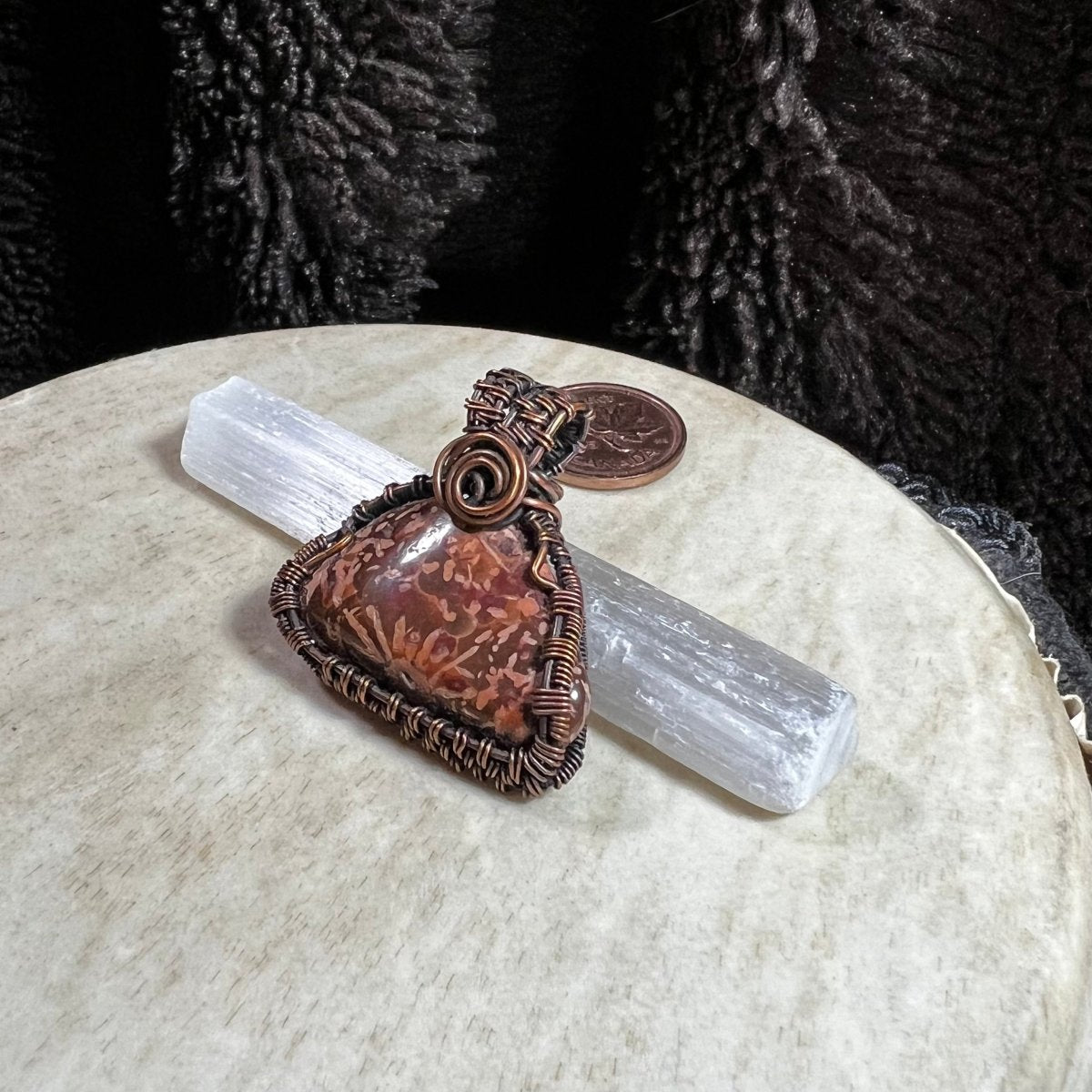 One-of-a-kind Starburst Jasper pendant wrapped in reclaimed copper wire displayed on a selenite wand with penny for size reference.