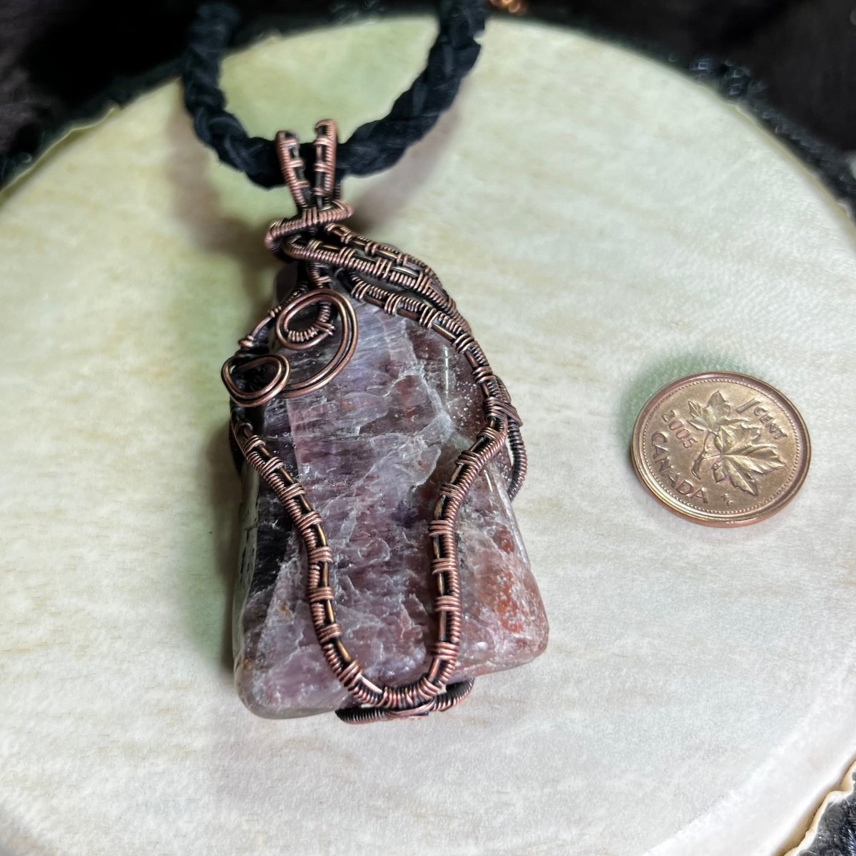 Necklace with a stone pendant and copper wire wrapping, next to a coin for scale, on a textured surface.