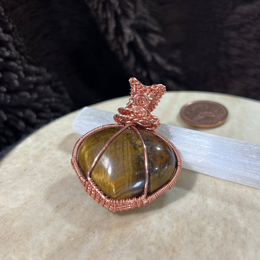 Pendant with tiger's eye stone and copper wire wrapping on a neutral background