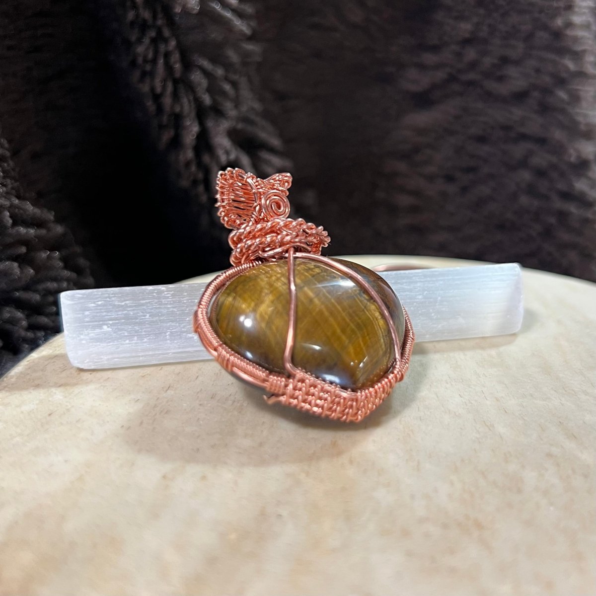 Copper-wrapped Tiger's Eye puffed heart pendant on a white surface with a dark textured background