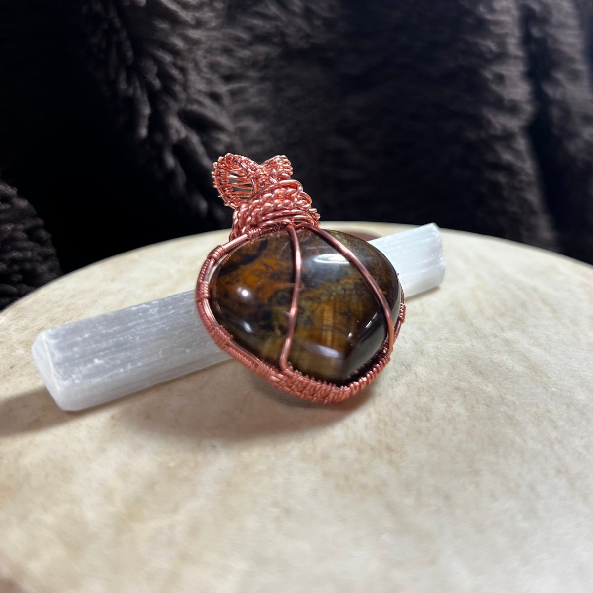 Copper-wrapped Tiger's Eye puffed heart pendant on a white surface with a dark textured background