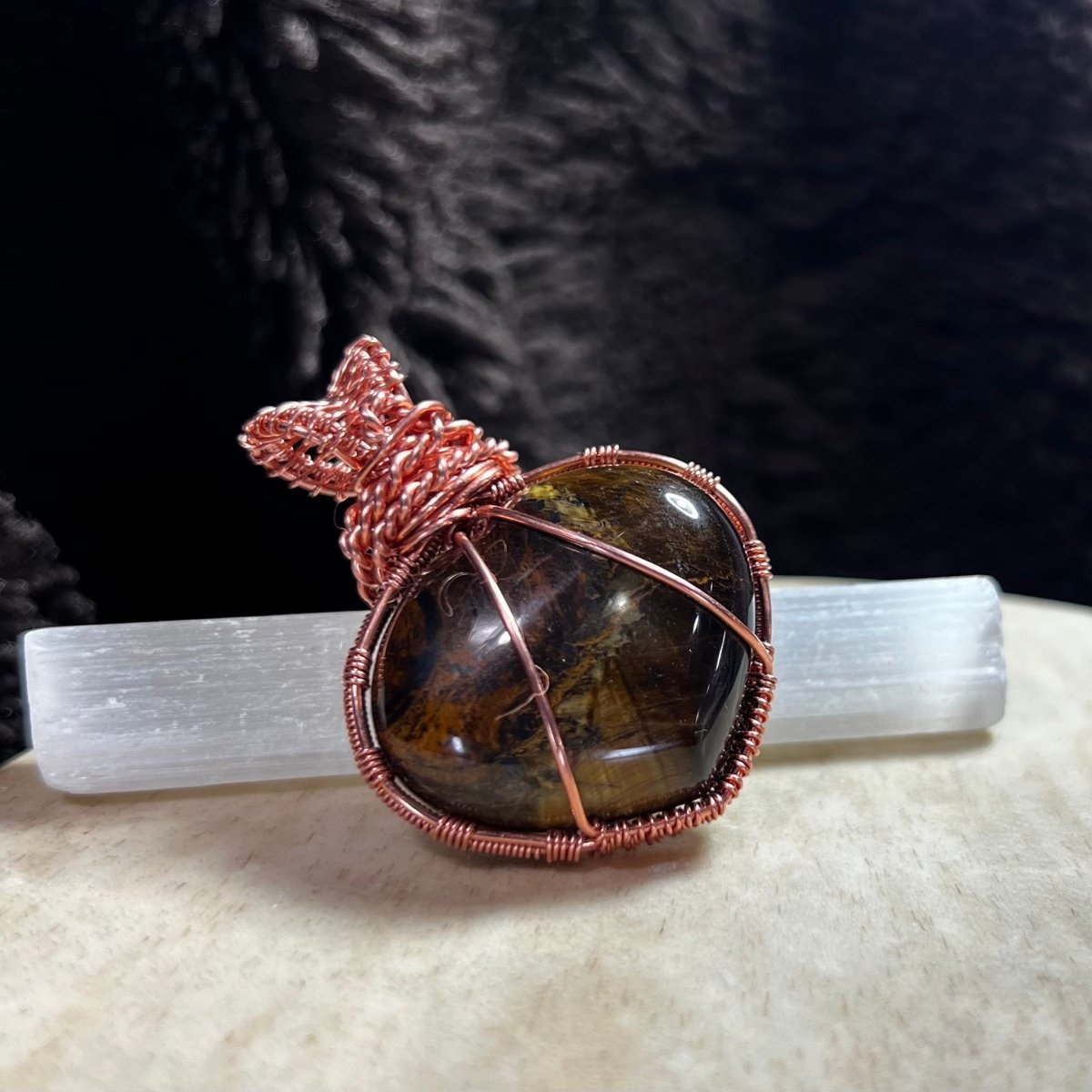 Copper-wrapped Tiger's Eye puffed heart pendant on a white surface with a dark textured background