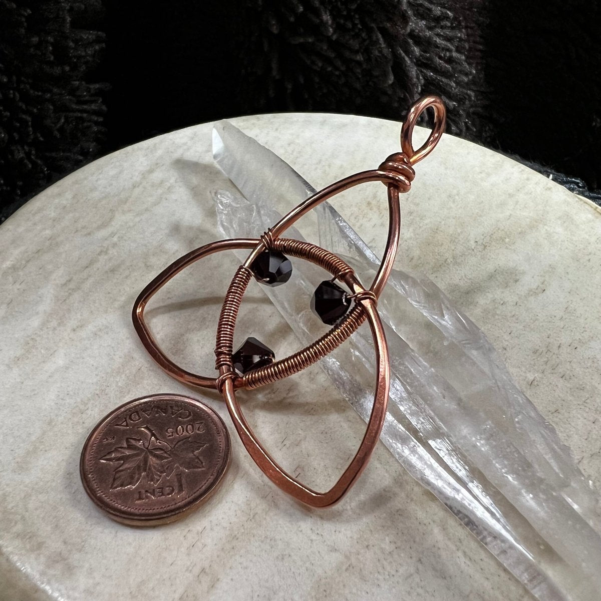 Copper wire-wrapped pendant with a penny on a beige surface